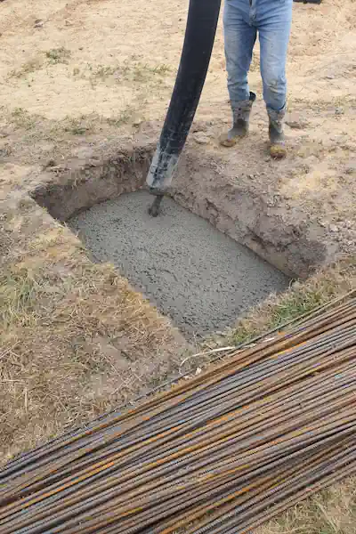 Builder standing beside an excavated trench filled with concrete next to stacked rebar for a slab foundation in Burleson TX