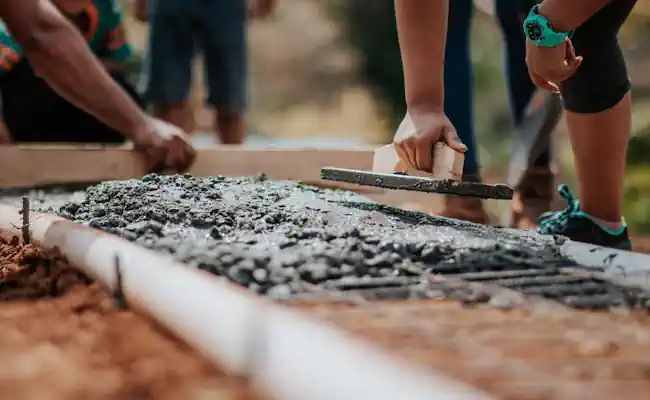 Worker using a hand trowel to finish fresh concrete beside forms during slab foundation construction in Burleson TX
